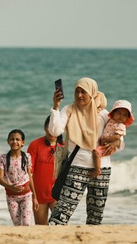A mother with her children enjoying a summer day at the beach, capturing memories with a smartphone.