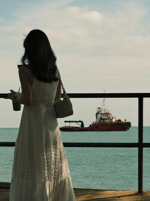 A woman in a white dress looking out at the water