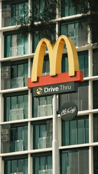Close-up of a McDonald's Drive Thru sign with a modern urban building in the background. 20209667