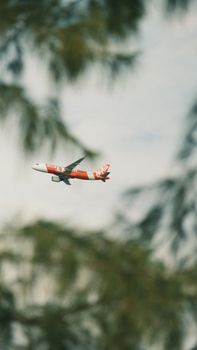 A bright red passenger airplane glides through the sky on a cloudy day, surrounded by blurred greenery.