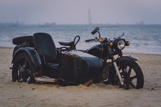 Rusty vintage motorcycle with sidecar parked on a sandy beach by the sea.