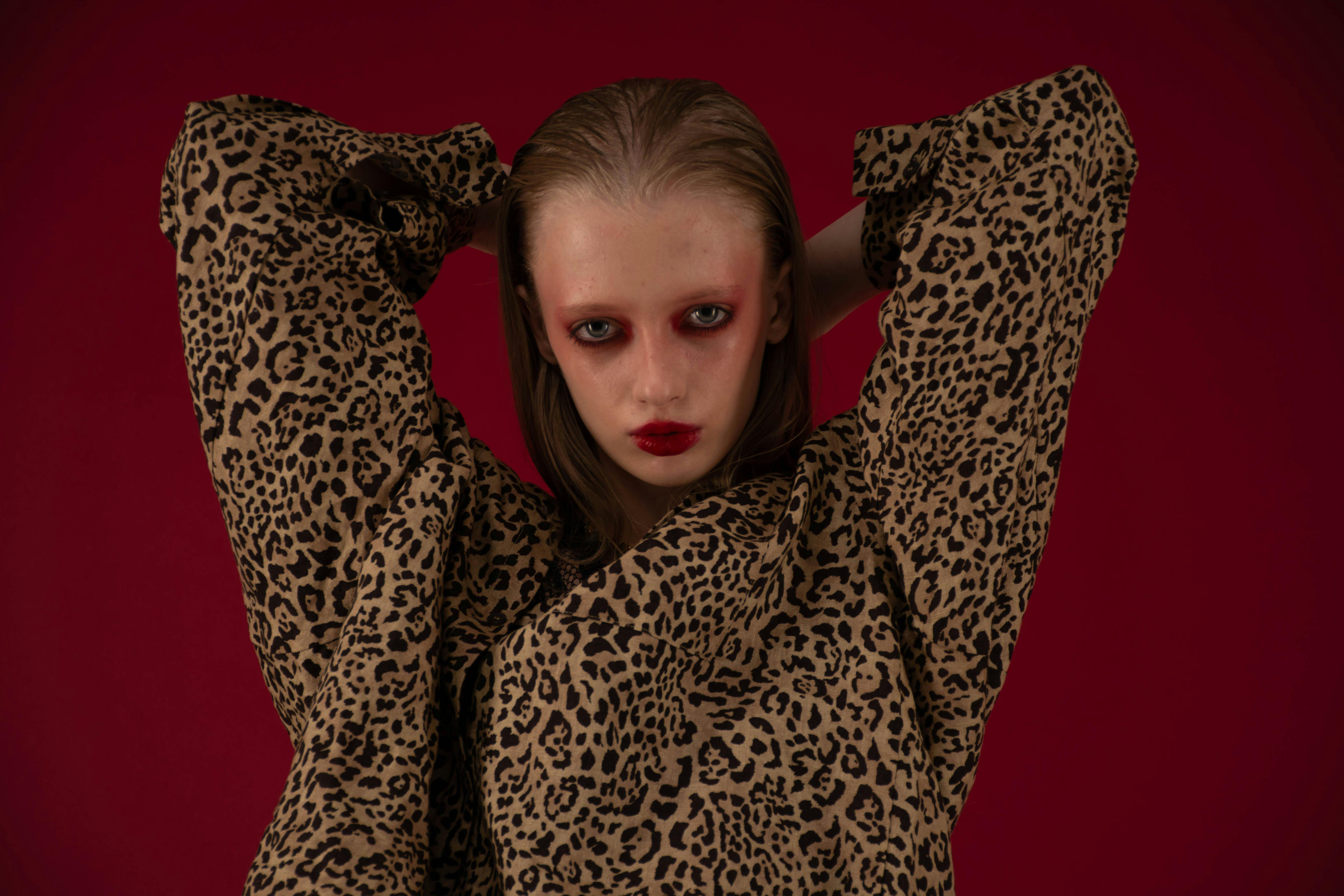 Striking portrait of a model in leopard print clothing with bold makeup in studio setting.