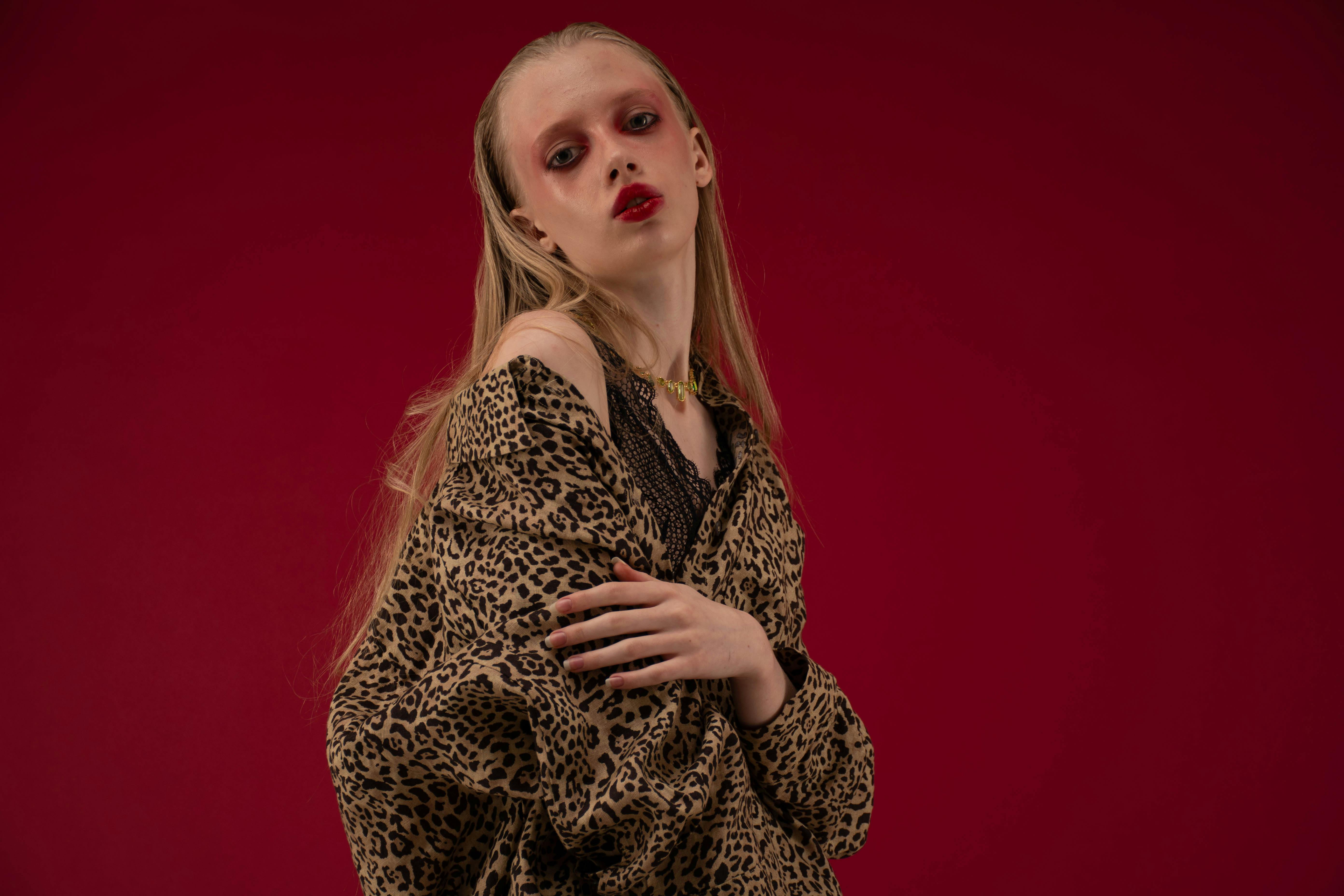 Elegant fashion model in leopard print against a bold red backdrop, showcasing striking makeup.