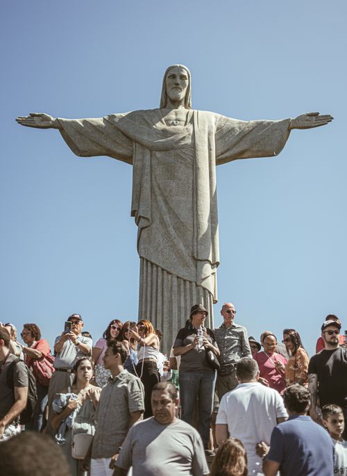 Free Iconic Christ the Redeemer statue in Rio de Janeiro with tourists gathered below under a clear sky. Stock Photo