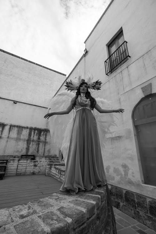 Black and White Photograph of a Woman Wearing a Costume, Standing on a Wall in a Patio