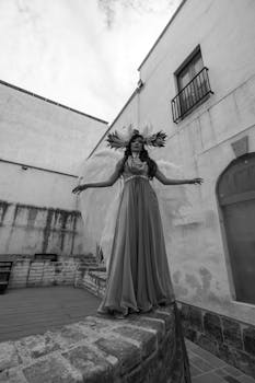 A woman in an elaborate fantasy costume poses dramatically in a rustic courtyard.