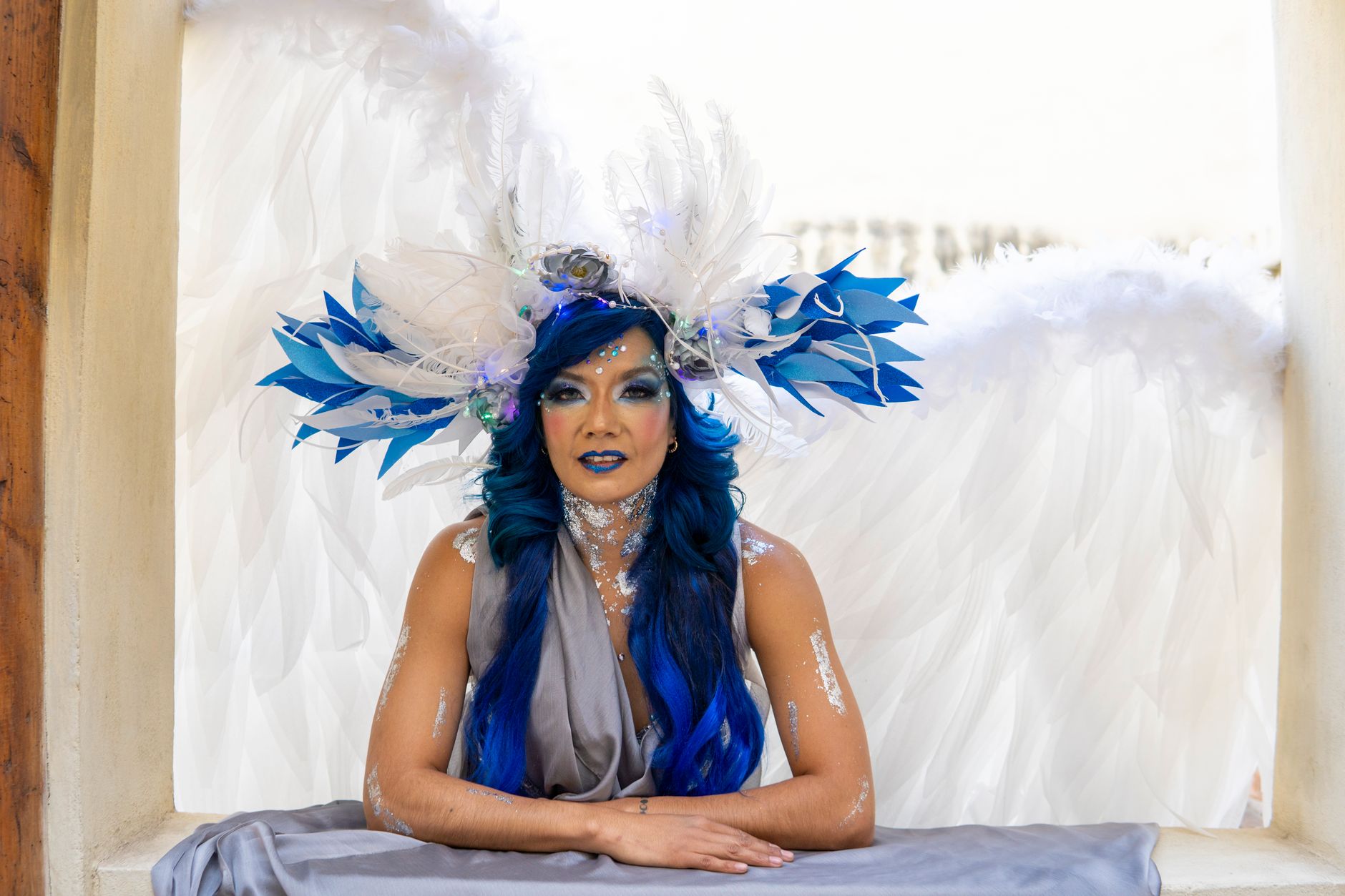 Stunning cosplay portrait featuring a woman with blue hair, wings, and a majestic feather headpiece.
