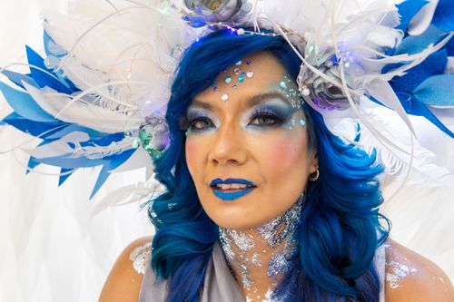 Free Captivating portrait of a woman with blue hair and a vibrant feathered headdress adorned with glitter and jewels. Stock Photo