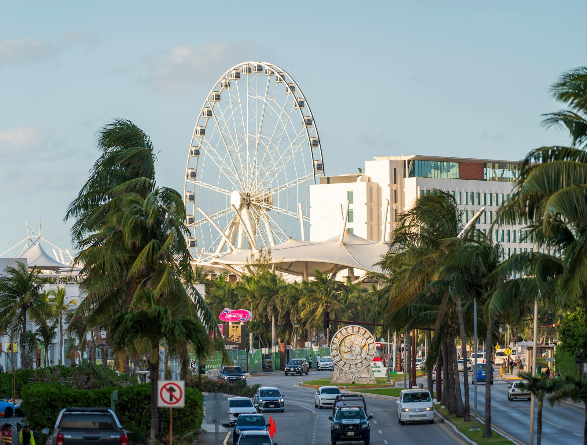 Cityscape of Cancun featuring a ferris wheel, palm trees, and modern buildings.