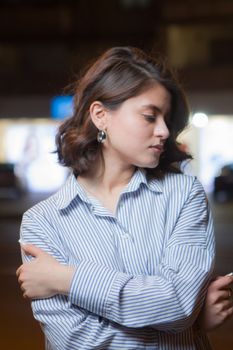 A fashionable woman wears a striped blouse with earrings under street lights at night.