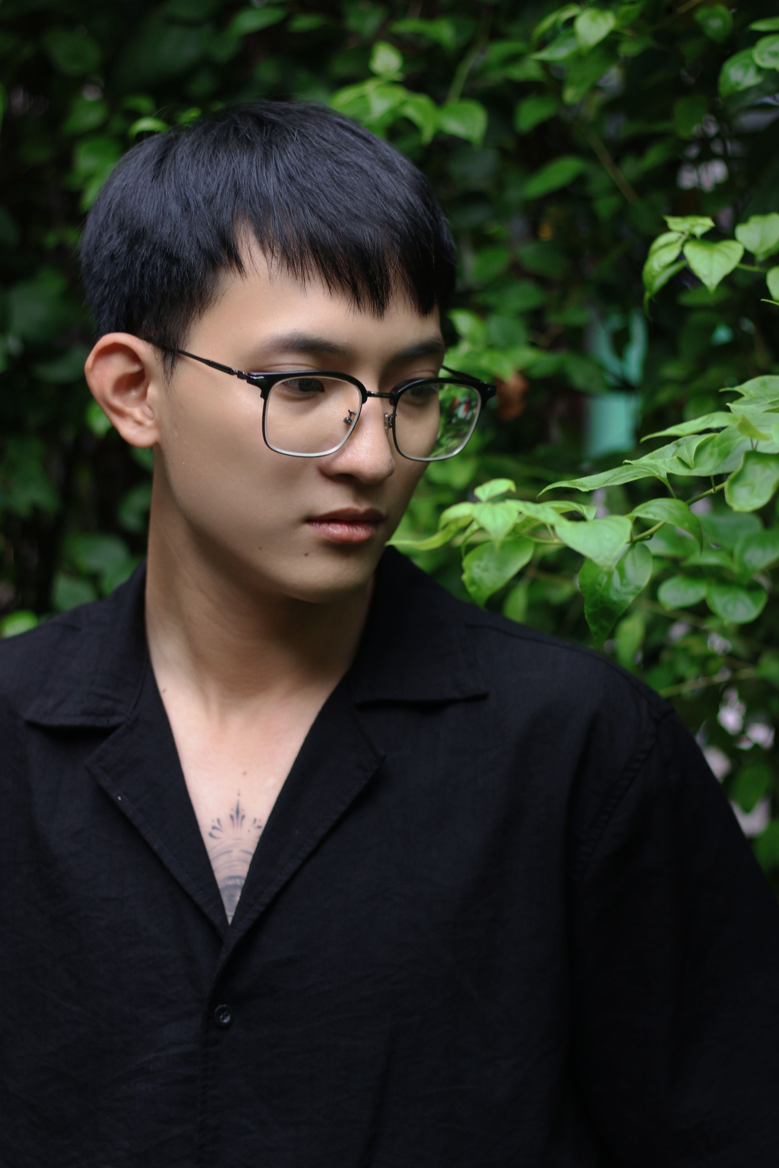 A serene portrait of a young man with eyeglasses in a green garden. Ideal for lifestyle themes.