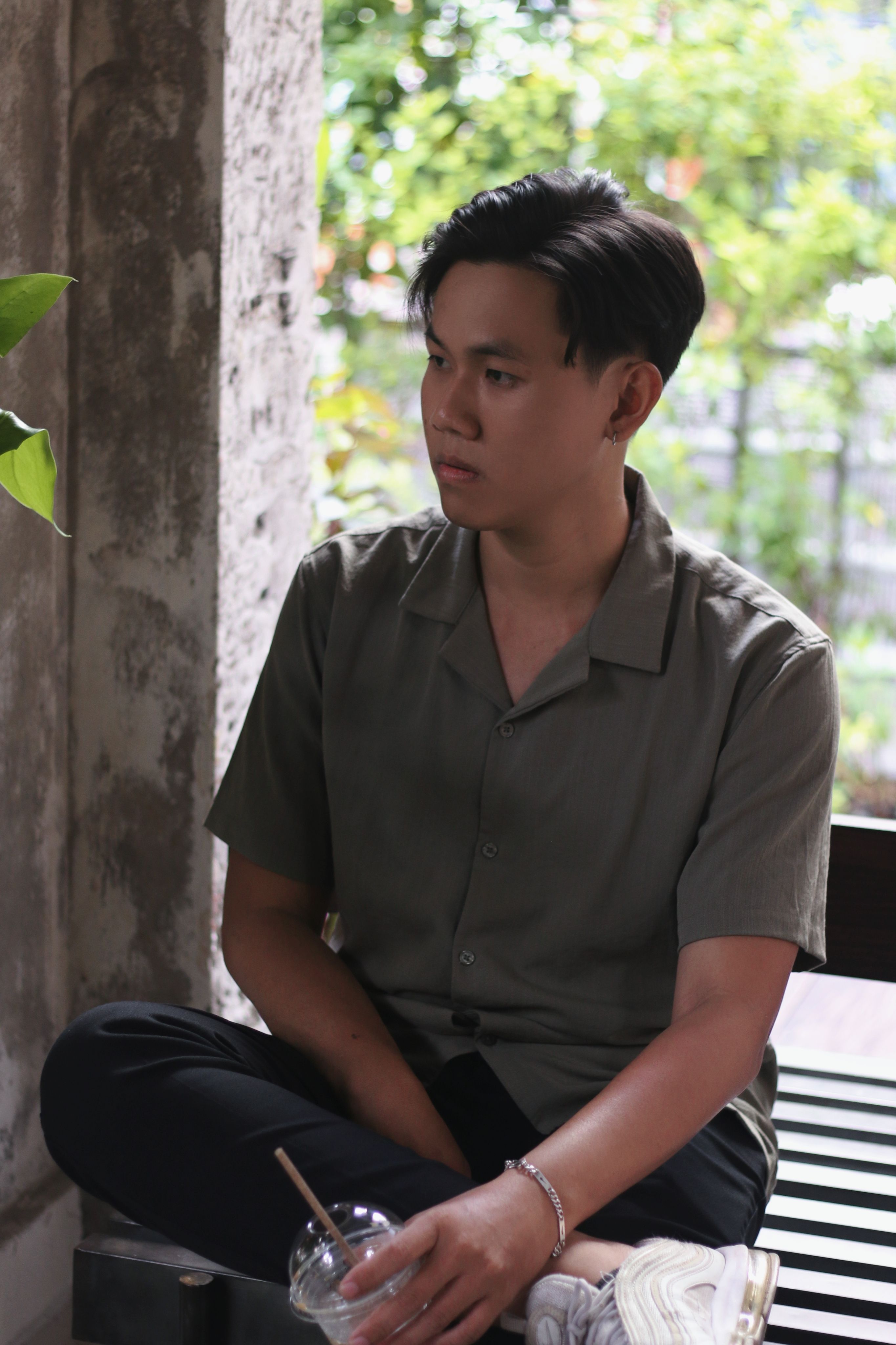 A young man sits by a window, enjoying a cold drink indoors during spring, looking pensive and relaxed.