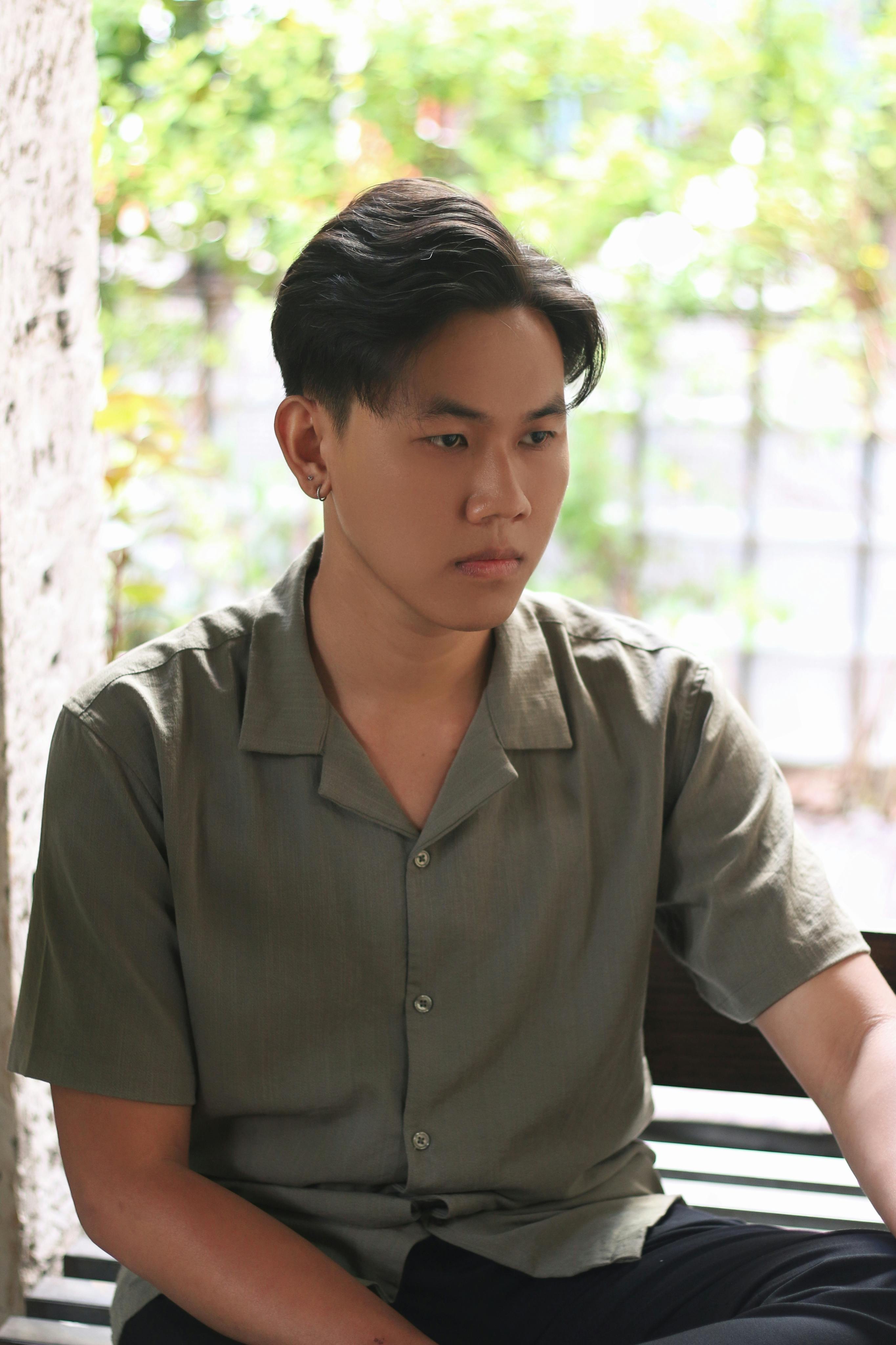 A thoughtful young man in a green shirt, sitting indoors near a window.