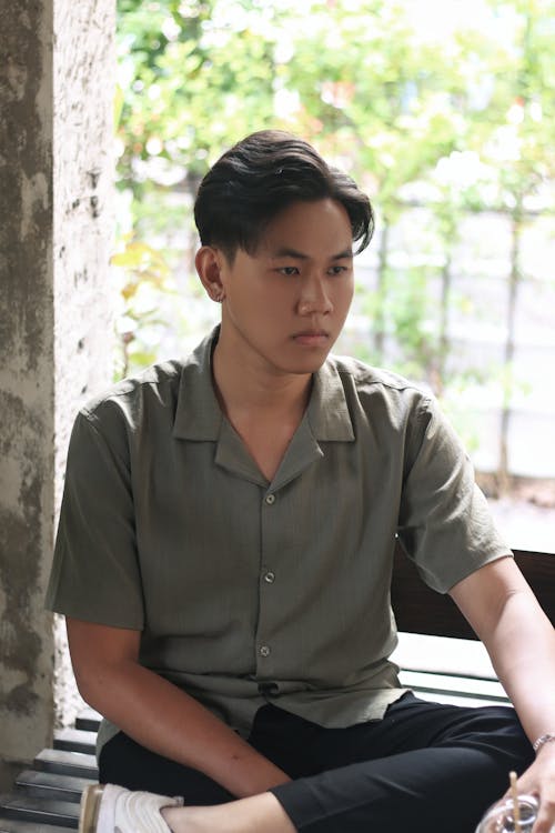 A Young Man in a Short Sleeve Shirt Sitting on a Bench in a Park 