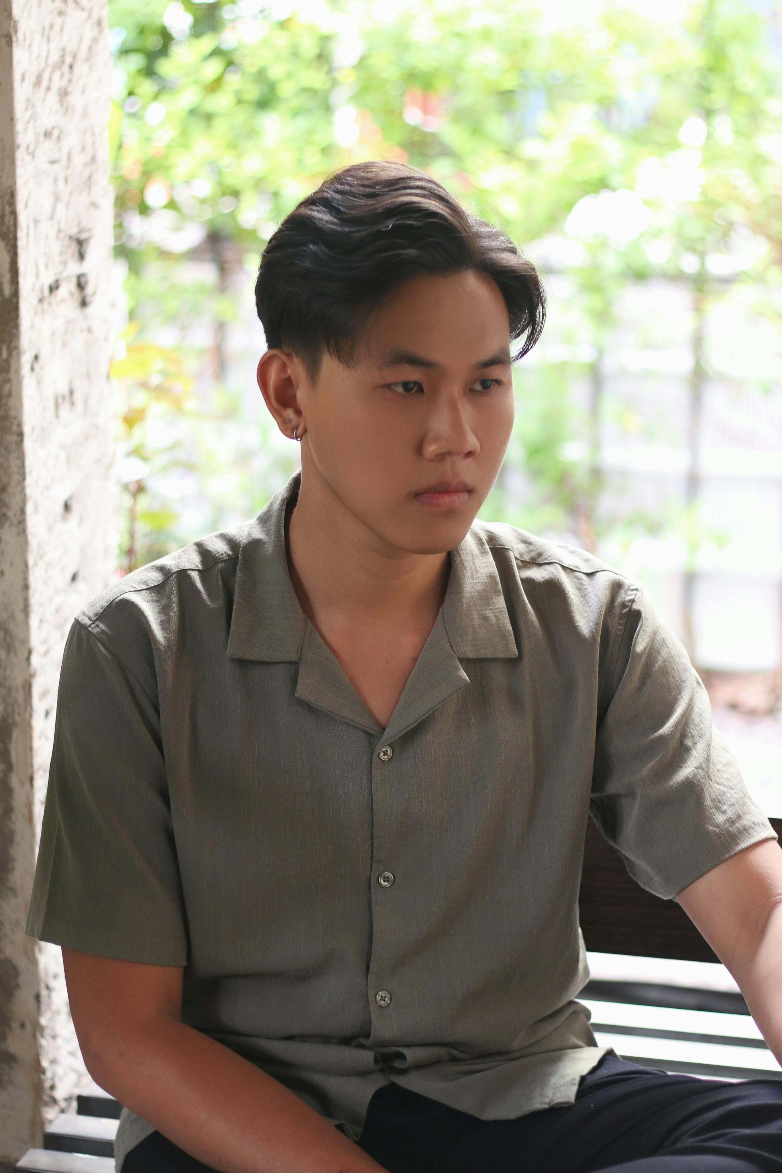 Pensive young man sitting indoors near a window with natural light.