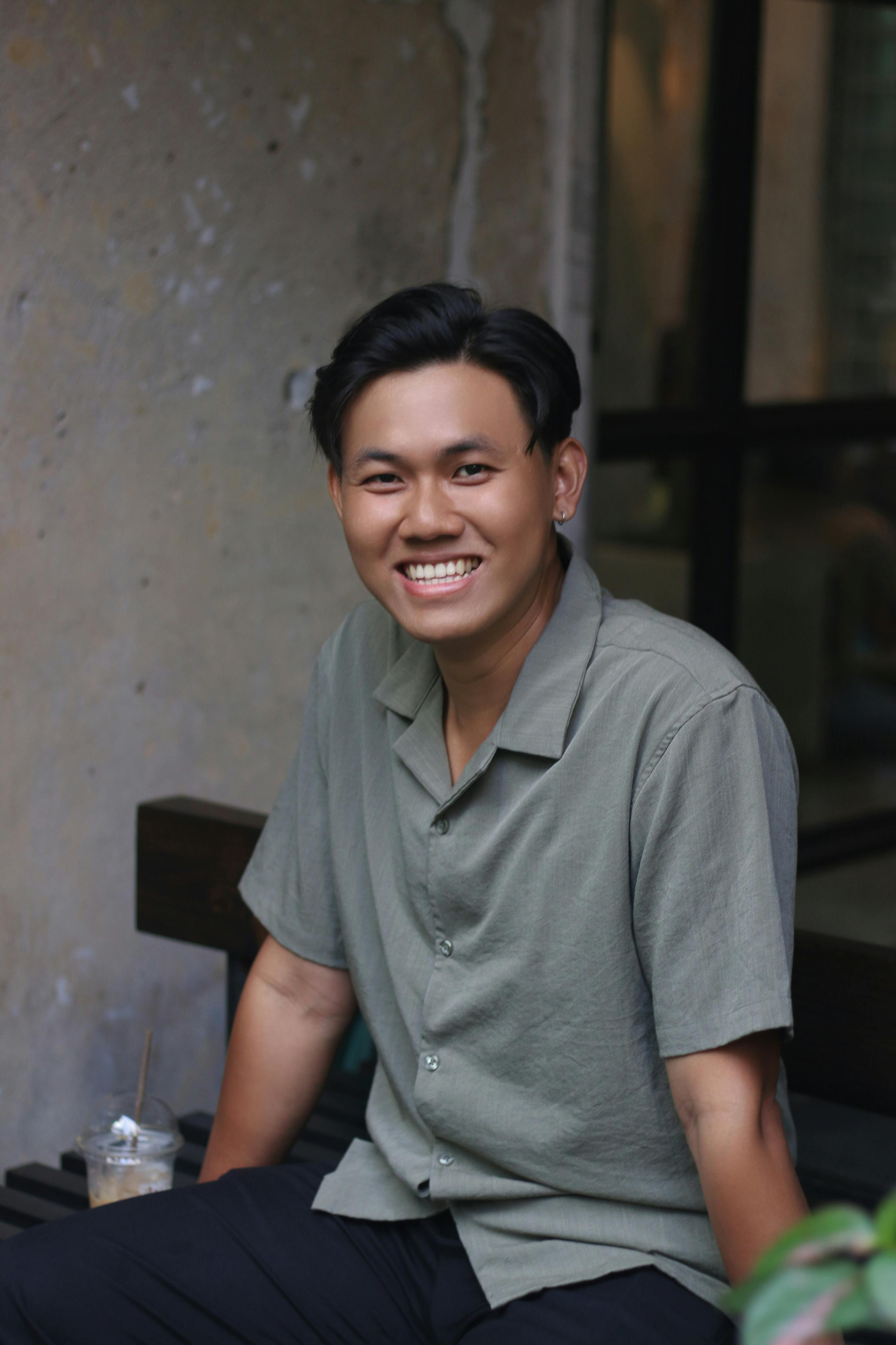 A cheerful young man in a casual shirt sitting indoors, showcasing a joyful expression.