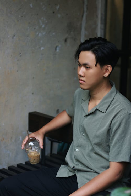 Young Man Sitting by a Wall with an Iced Coffee