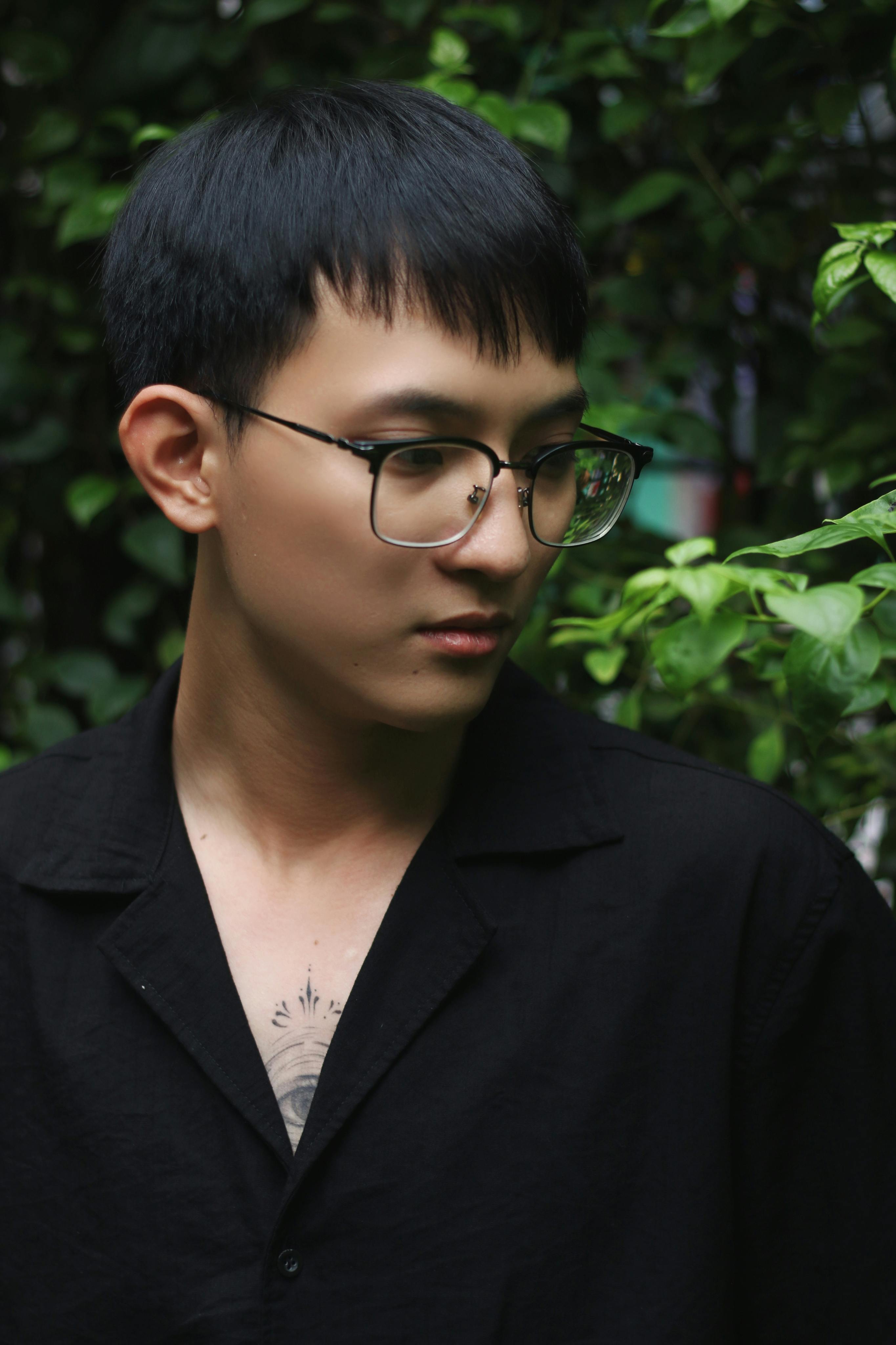 Serene portrait of a young man in glasses surrounded by green foliage.