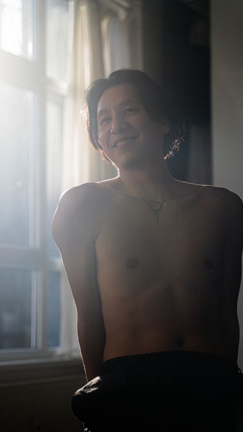 Free A shirtless man smiles warmly in a sunlit room, capturing a moment of natural beauty. Stock Photo