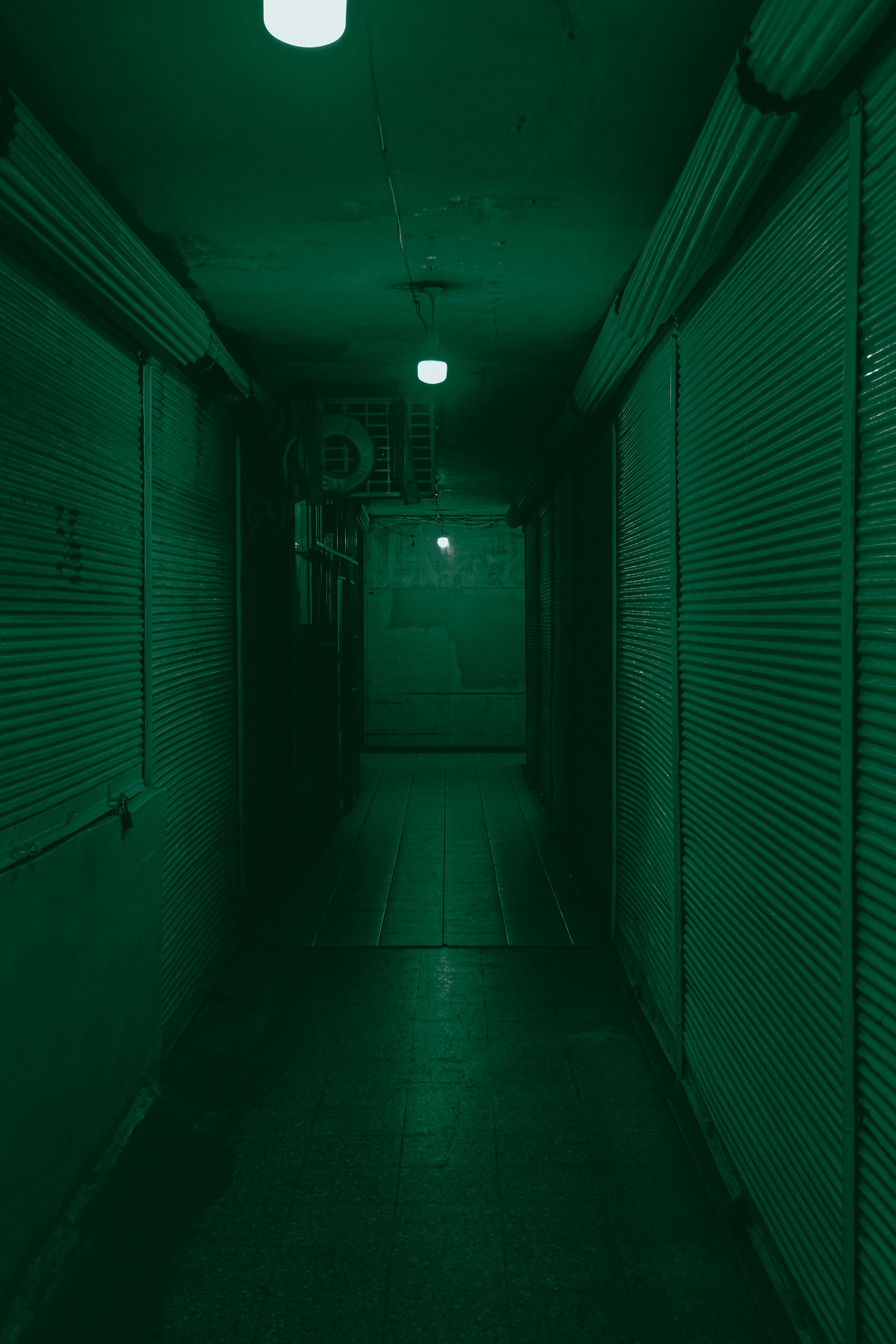 Explore the eerie shadows of an abandoned alley with closed shutters and dim lights.