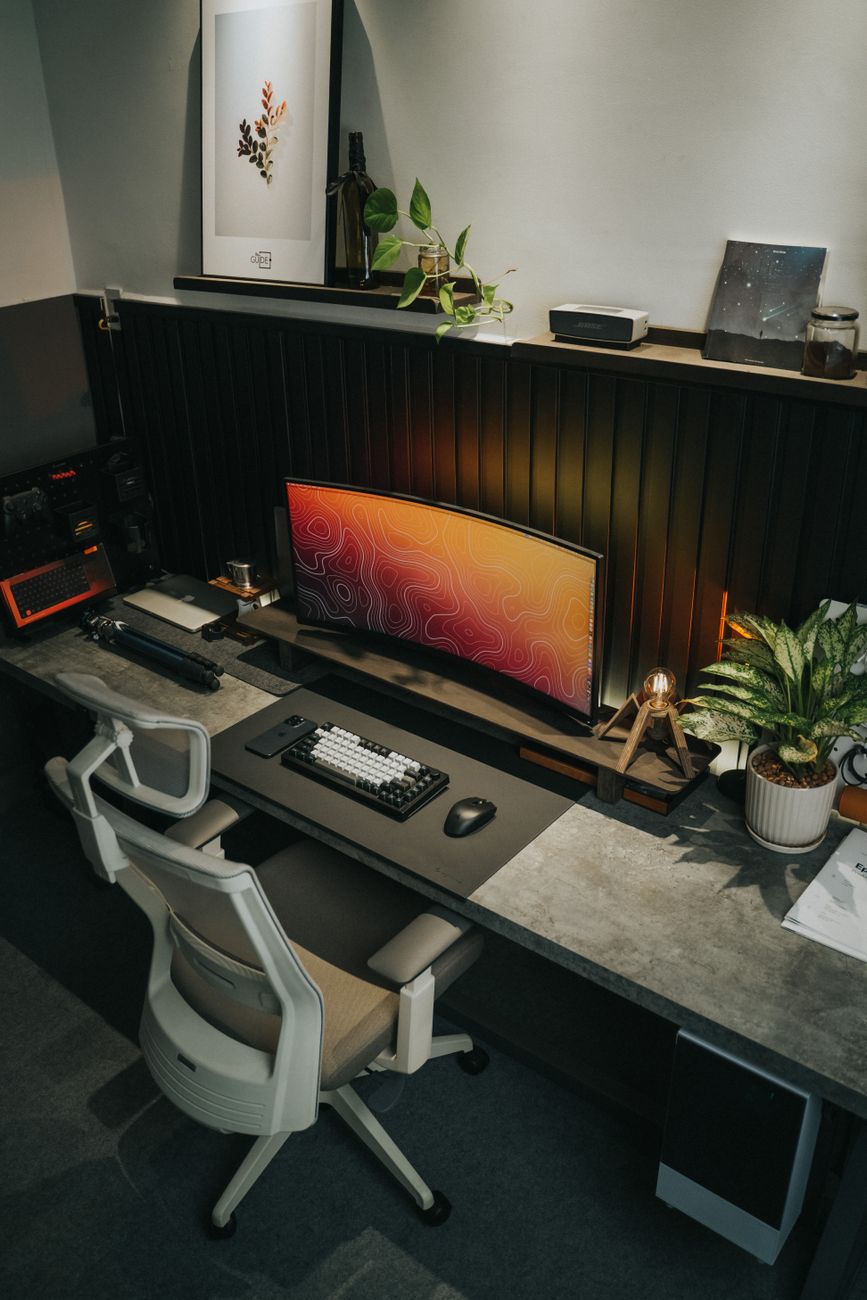 A stylish office desk setup with a curved monitor, ergonomic chair, and plants.