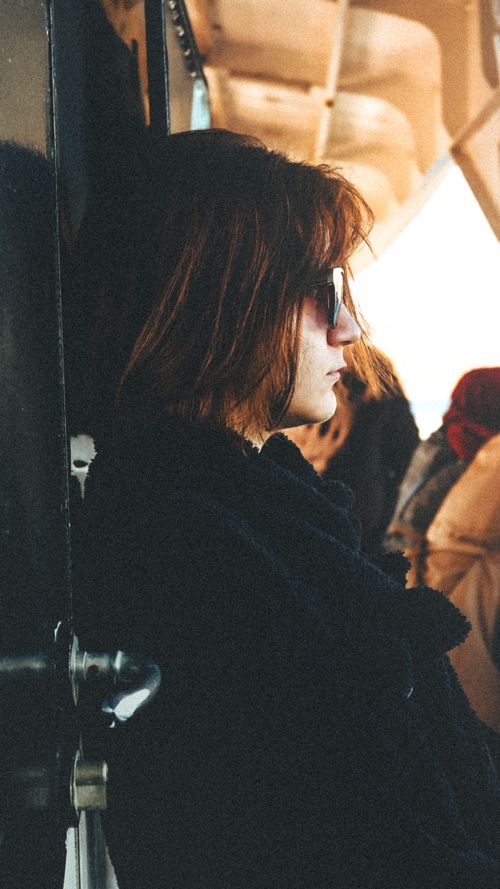 Free Profile of a stylish woman with short hair wearing sunglasses, leaning against a door in a casual setting. Stock Photo