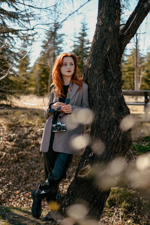 Pretty Redhead Wearing a Gray Coat Leaning on a Tree