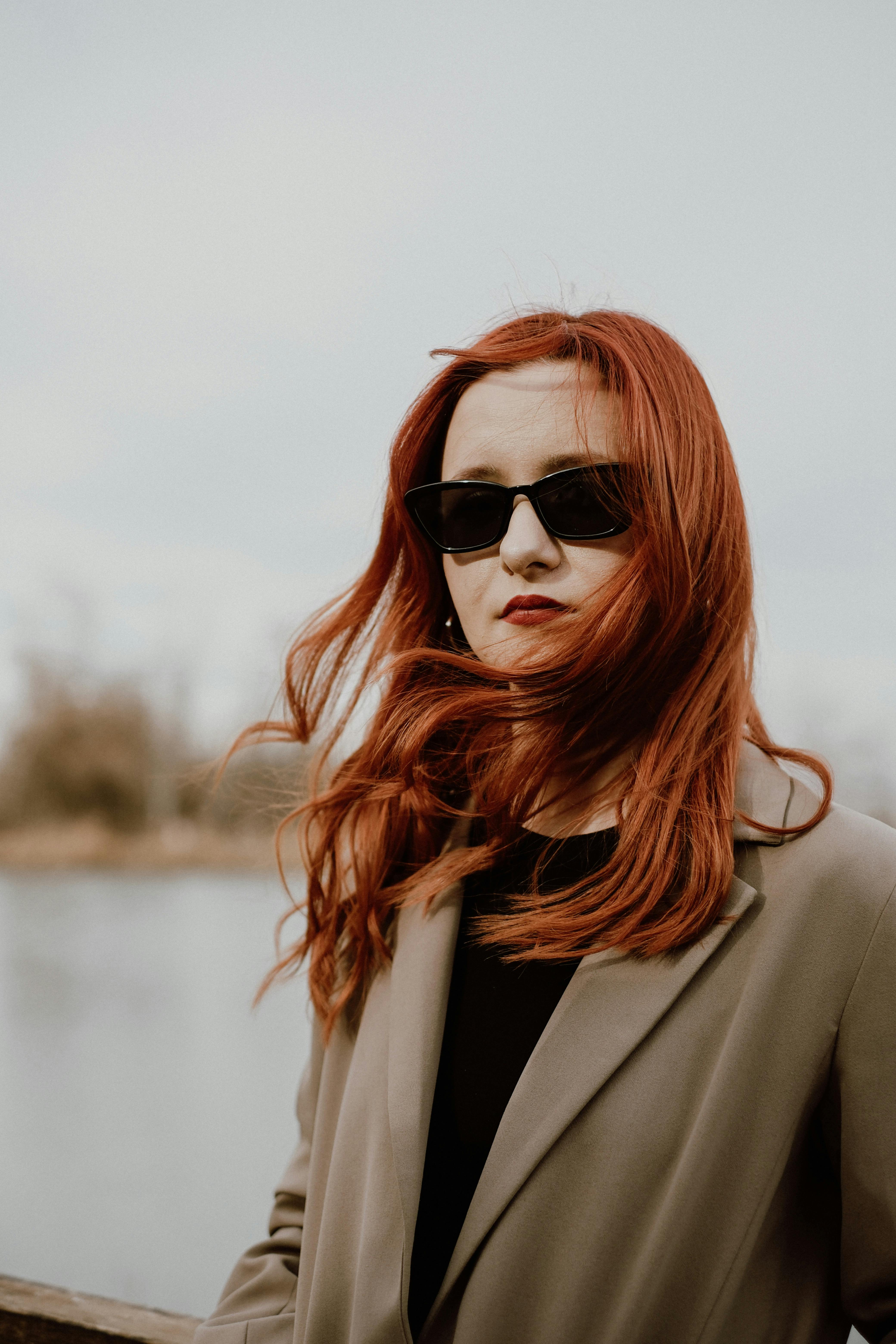 Portrait of a redhead woman with sunglasses in a gray coat, showcasing fashion outdoors.