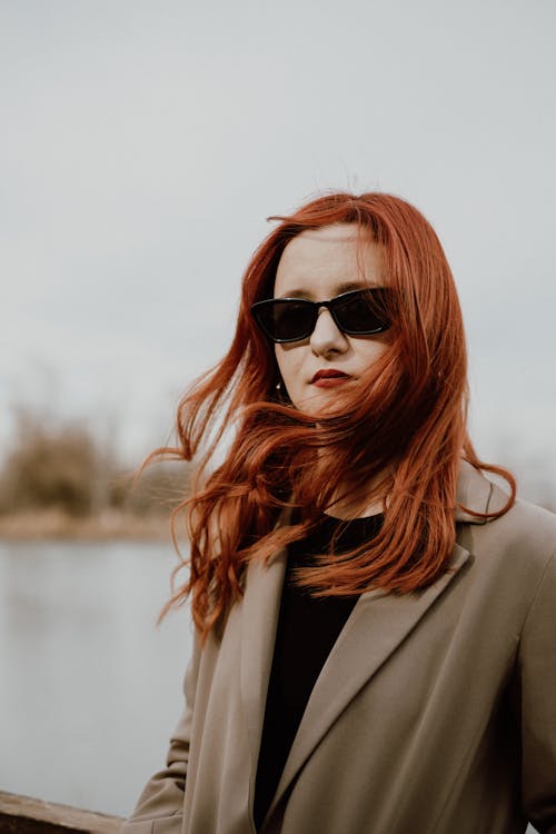 A woman with red hair wearing sunglasses and a coat
