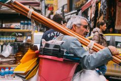 Elderly man carries cleaning tools in vibrant city street market, showcasing urban hustle.