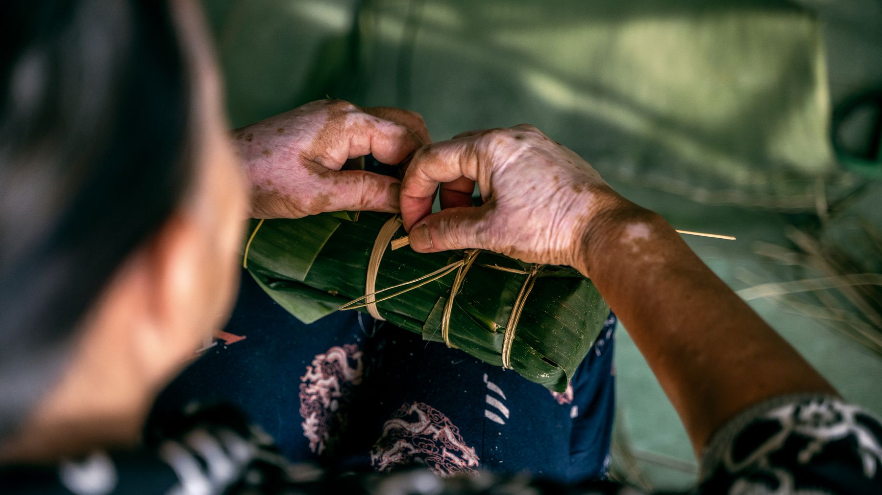 Close-up of hands skillfully wrapping Banh Tet with banana leaves, showcasing traditional Vietnamese preparation.