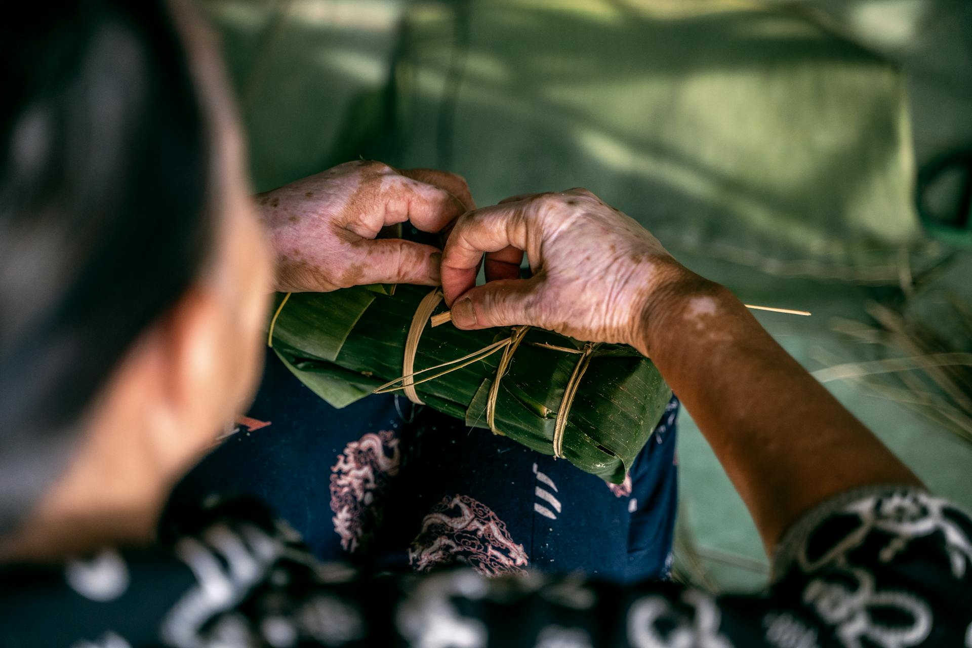 Close-up of hands skillfully wrapping Banh Tet with banana leaves, showcasing traditional Vietnamese preparation.