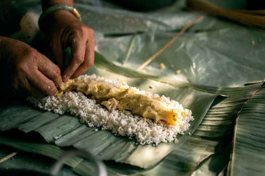 Hands preparing traditional Vietnamese sticky rice cake on banana leaves, showcasing cultural cuisine.