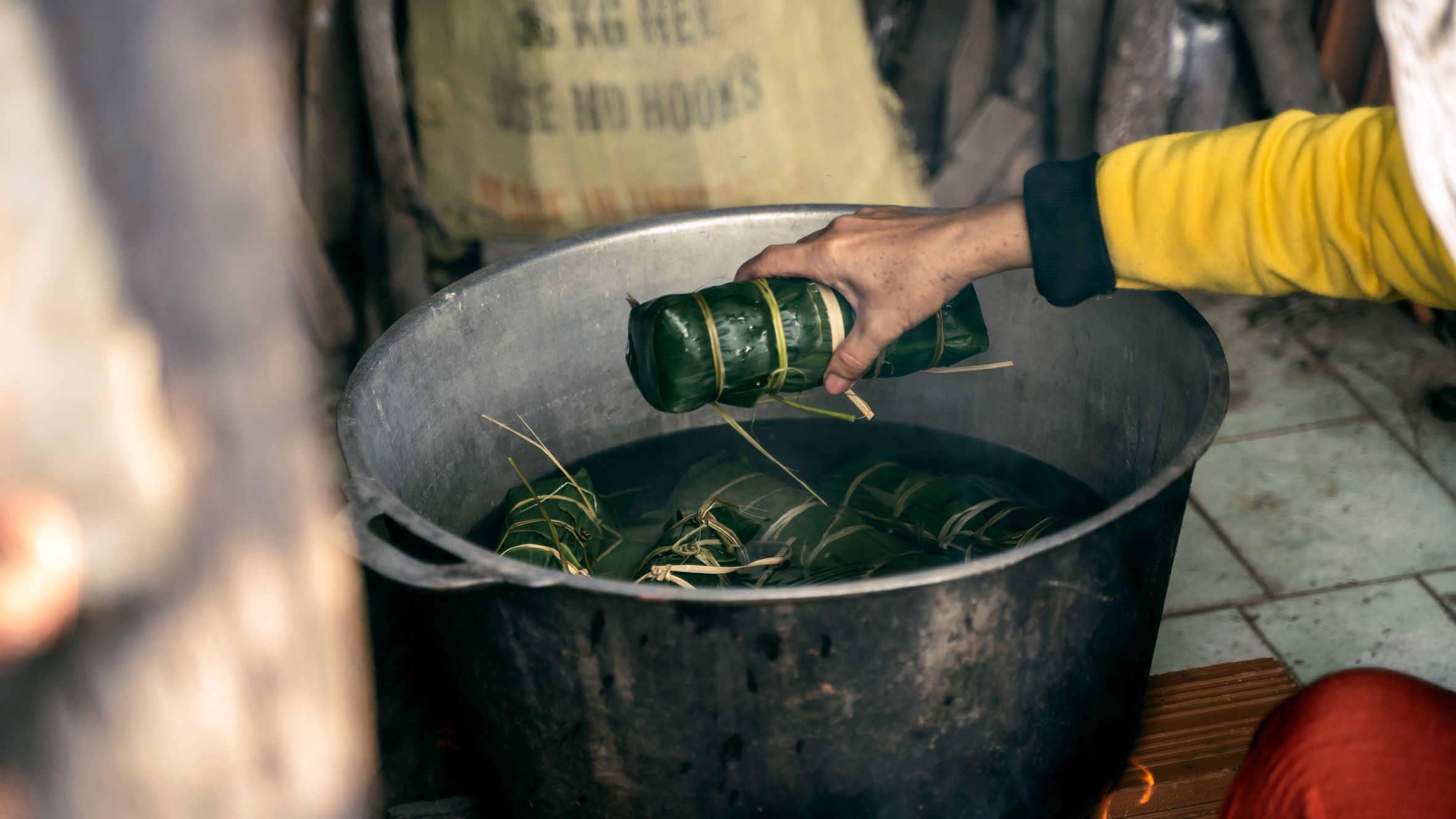 A person preparing Vietnamese banh tet by boiling wrapped rice cakes in a rustic kitchen setting.