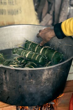 Close-up of hands preparing traditional Vietnamese banh tet in an outdoor setting over an open flame.