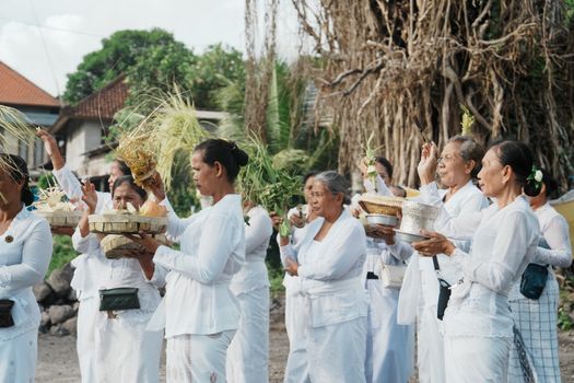 Balinese women dressed in white participate in a traditional outdoor ceremony.