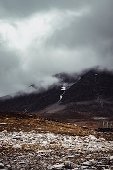 Explore the moody mountain landscape shrouded in fog and mist under stormy skies.
