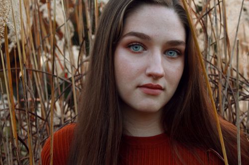 Free A woman with striking blue eyes poses amidst dry reeds and foliage. Stock Photo