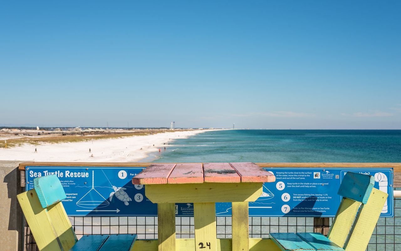 Vibrant table and chairs overlooking the serene Navarre Beach, Florida coastline under a clear blue sky.