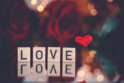 Free Scrabble tiles spelling 'Love', surrounded by red roses and a heart. Perfect for Valentine's Day. Stock Photo