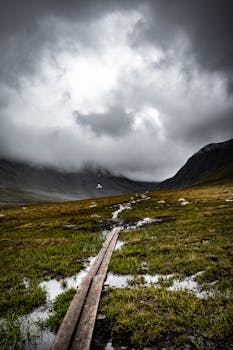 Dramatic cloudy mountain landscape with a narrow wooden trail and misty weather.