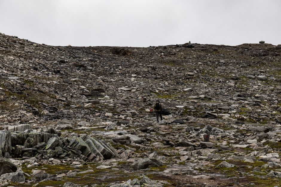 Amazing All-inclusive Northern Lights Hunt Review: An Unforgettable Norway Expedition Review 2026 - A lone person hikes across a desolate rocky landscape under a cloudy sky.
