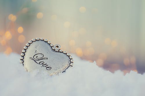 A heart shaped silver pendant sitting in the snow