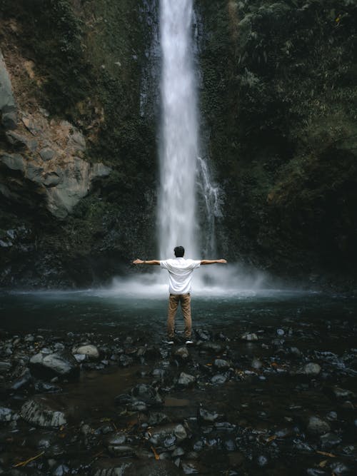 Man Standing with Arms Stretched by Waterfall