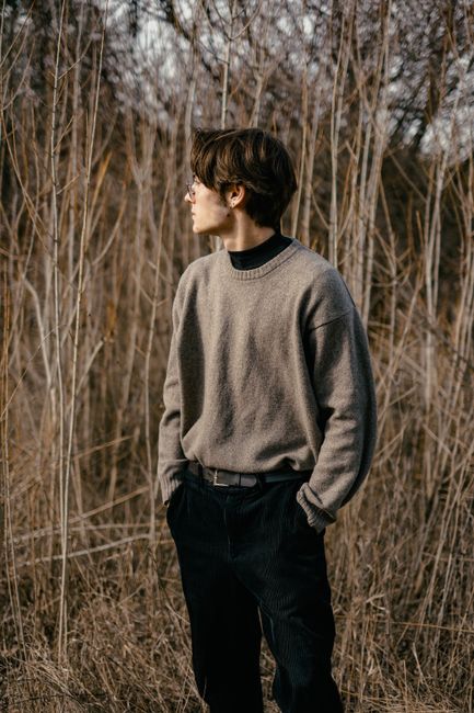 Casual portrait of a stylish young man in a serene autumn setting, wearing a gray sweater.