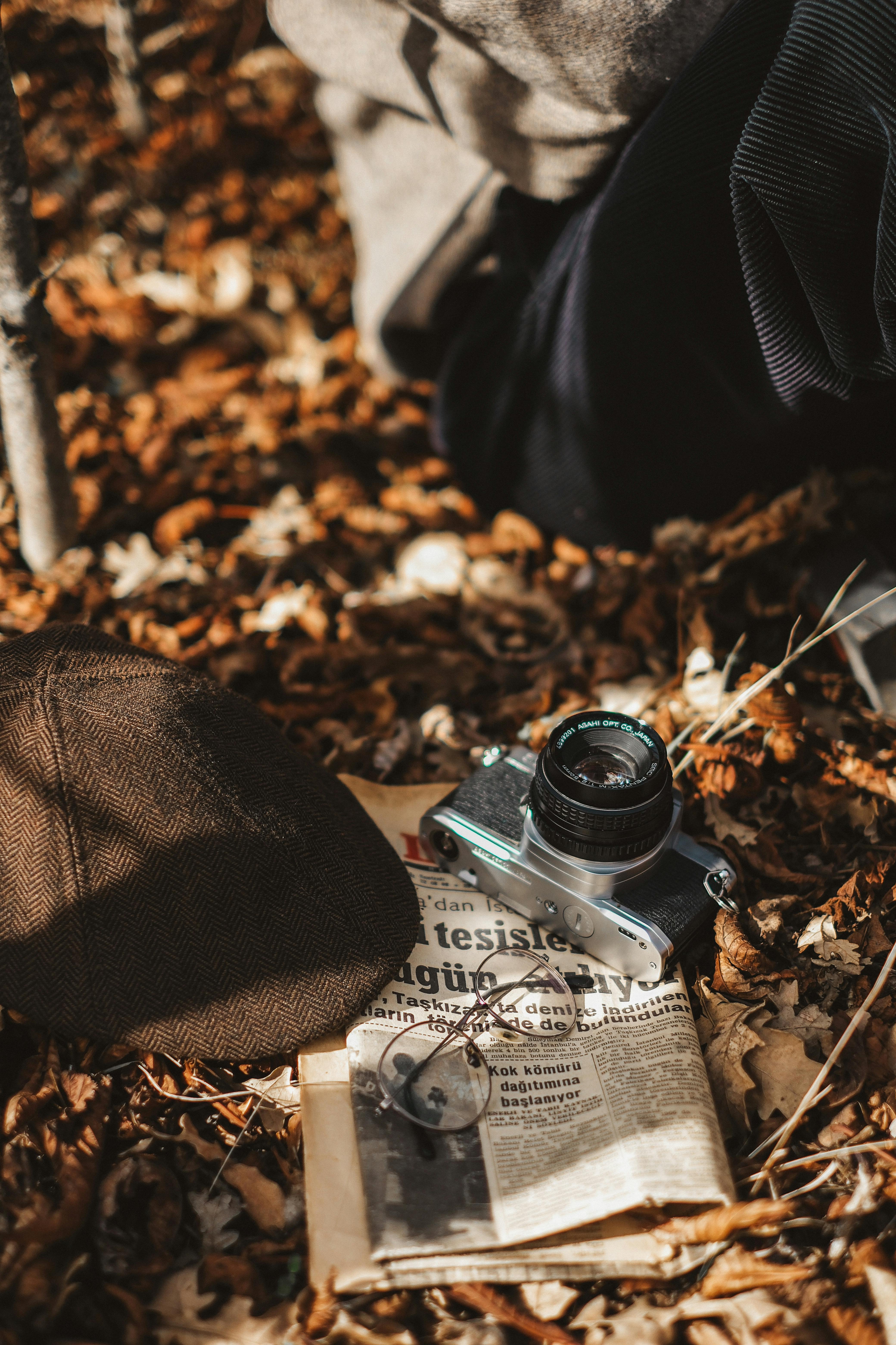 A retro camera and newspaper on autumn leaves, evoking nostalgia.