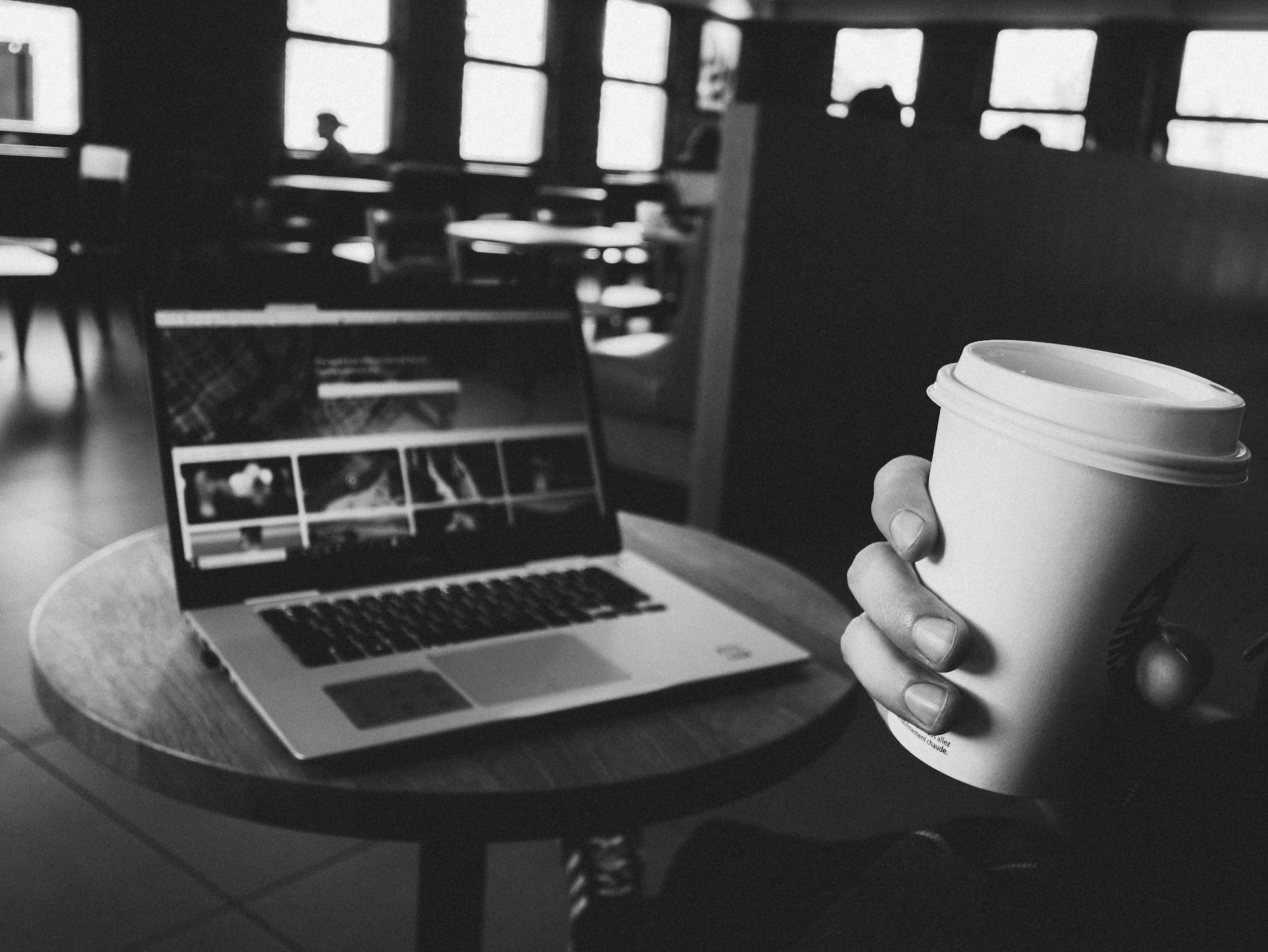 A cozy coffee shop scene with a laptop and coffee cup on a table, perfect for tech and lifestyle themes.