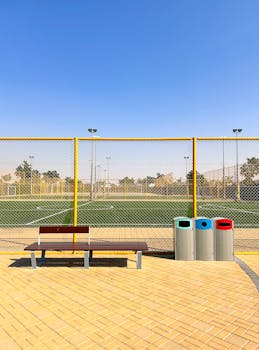 A bright day at a Dubai soccer field showing benches, trash bins, and a blue sky, highlighting urban recreation.