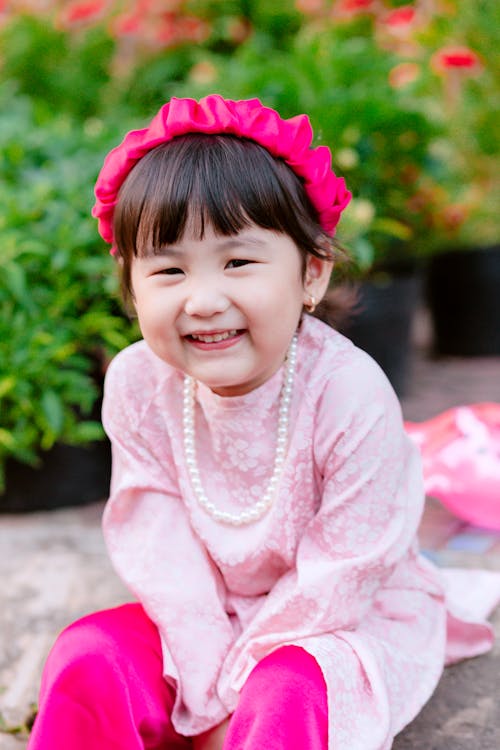 A little girl wearing pink and pink pearls sitting on the ground