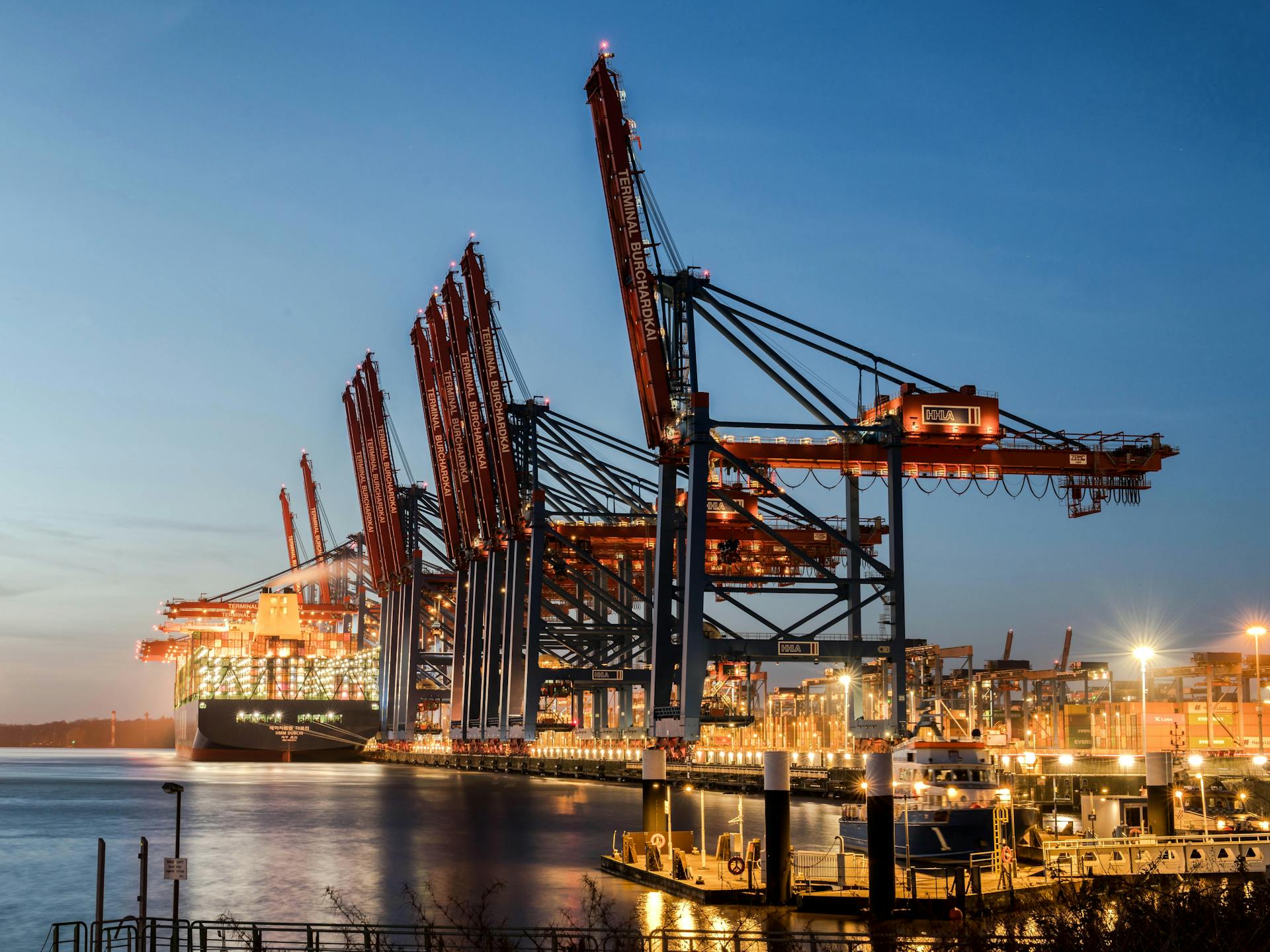 Industrial port scene at Hamburg with illuminated cranes and container ships during dusk.